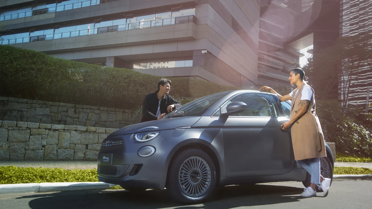 Fiat 500e estacionado ao lado de uma mulher em ambiente urbano.